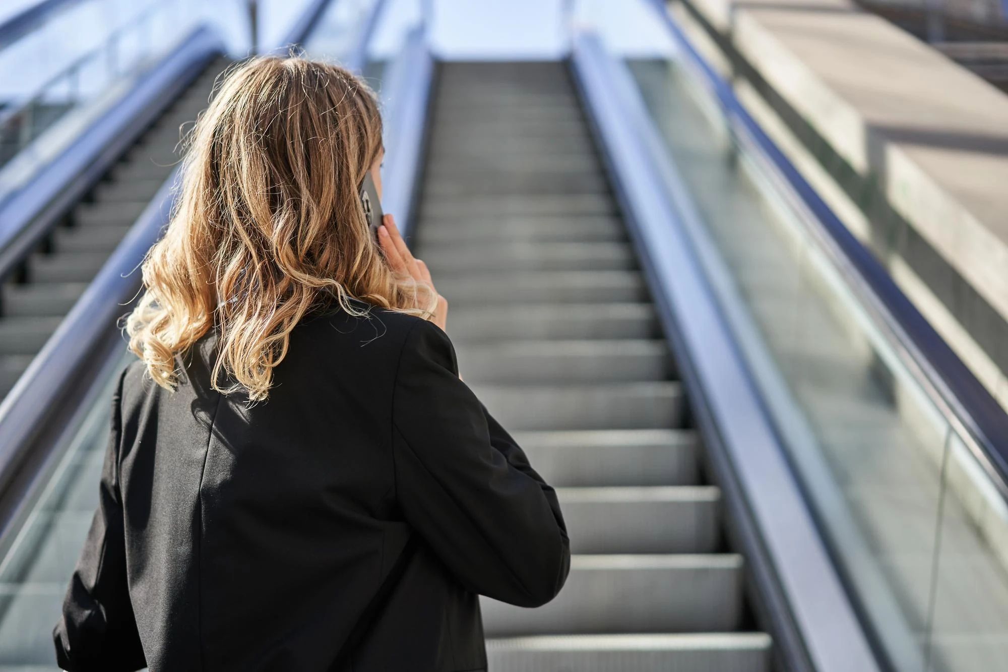 Säljare i telefon på väg uppför en rulltrappa
