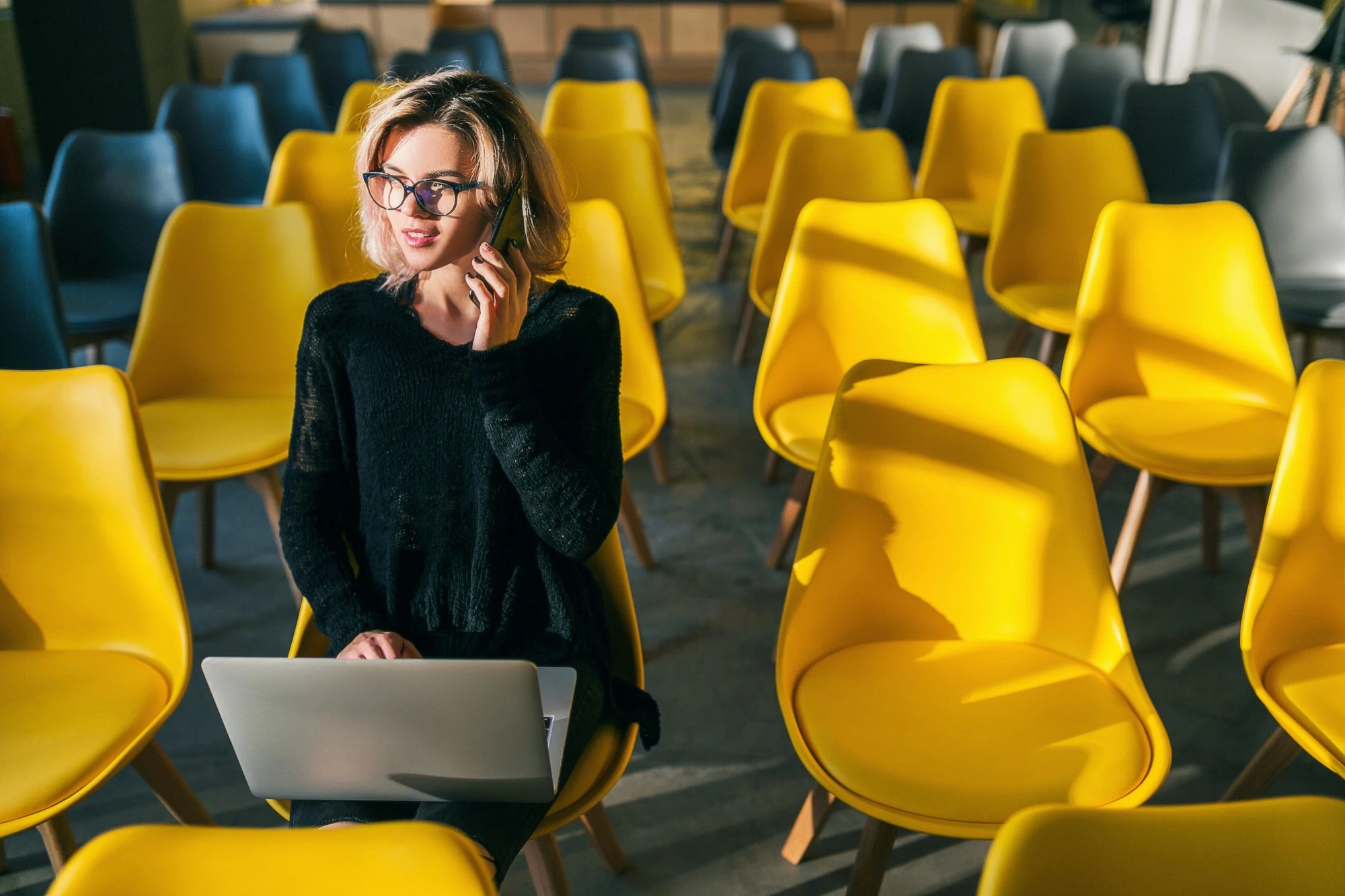 Säljare som ringer med laptop i knät bland gula stolar